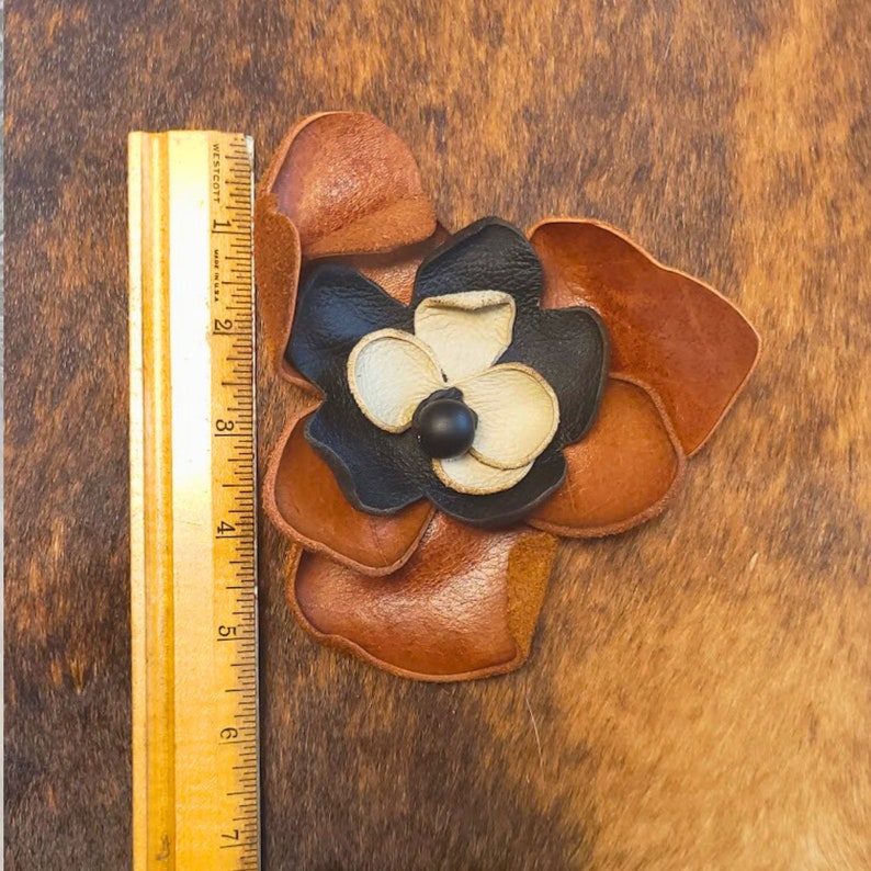 May include: A brown leather flower with black and white petals. The flower is about 3 inches wide.