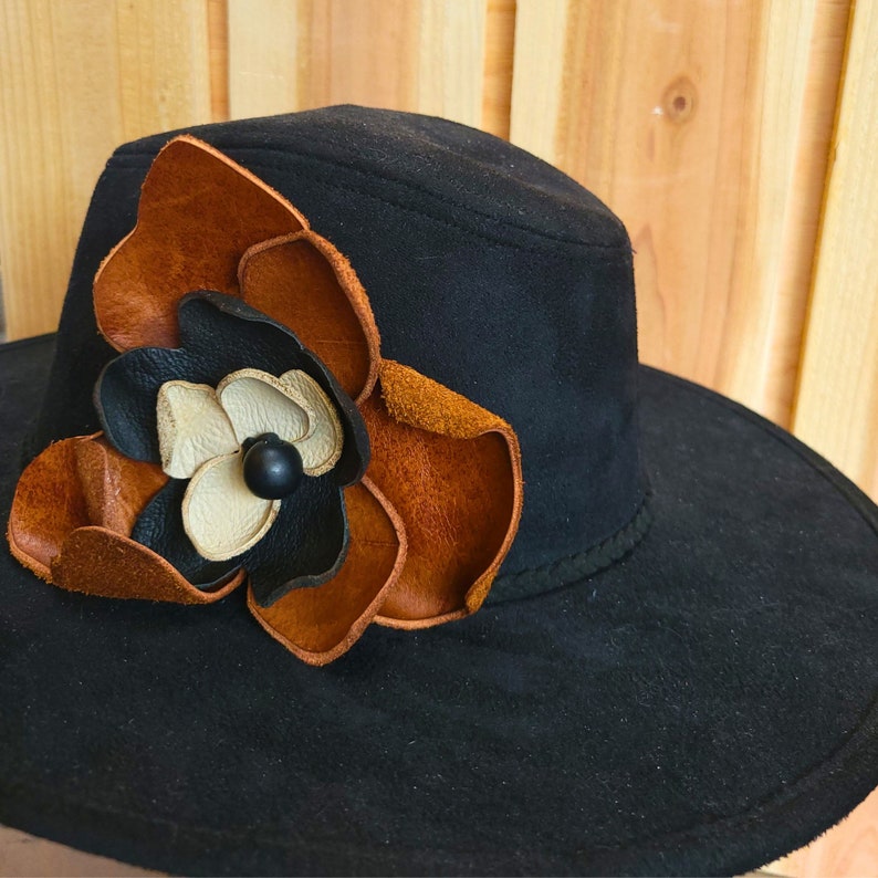 May include: A black wide-brimmed hat with a large brown, black, and white leather flower accent.