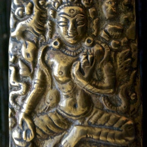 May include: A brass sculpture of a deity with intricate details and a serene expression. The sculpture is set against a background of floral and geometric patterns.