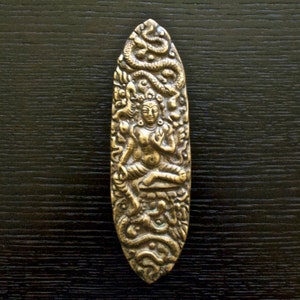 May include: A gold-coloured metal pendant depicting a deity sitting in a lotus position, surrounded by intricate carvings of snakes and other mythical creatures.