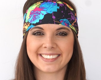 May include: A woman with long brown hair is wearing a black headband with a colorful floral print. The headband has a splatter paint design with bright pink, blue, green, and yellow colors.