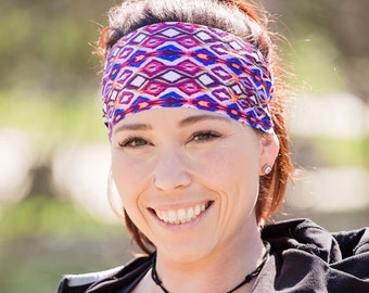 May include: A woman with brown hair wearing a black jacket and a colorful headband. She is smiling and wearing a necklace with a blue stone pendant.