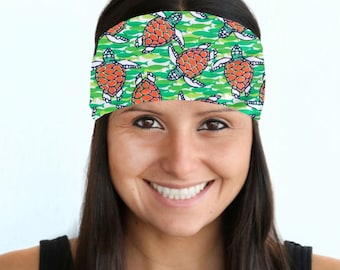 May include: A woman with long dark hair is wearing a green and white headband with a pattern of orange sea turtles. The headband is made of a soft, stretchy material and is perfect for keeping hair out of the face.