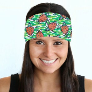 May include: A woman with long dark hair is wearing a green and white headband with a pattern of orange sea turtles. The headband is made of a soft, stretchy material and is perfect for keeping hair out of the face.