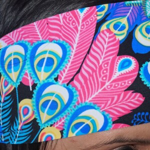 Peut inclure: Un bandeau noir avec un motif de plumes de paon color&eacute;. Le bandeau pr&eacute;sente des plumes roses, bleues, vertes et jaunes.
