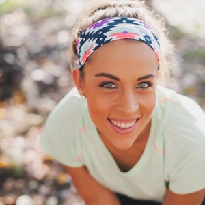 May include: A woman with brown hair wearing a green shirt and a colourful headband with a geometric pattern. She is smiling and looking at the camera.