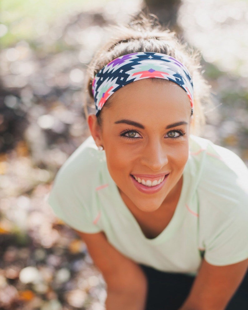 May include: A woman with brown hair wearing a green shirt and a colourful headband with a geometric pattern. She is smiling and looking at the camera.