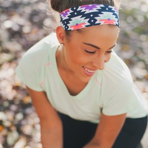 May include: A woman wearing a green shirt and black trousers with a colourful patterned headband. The headband has a geometric design with pink, blue and white accents.