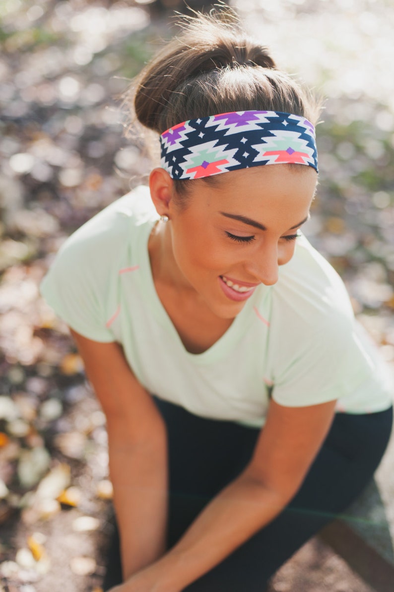 May include: A woman wearing a green shirt and black trousers with a colourful patterned headband. The headband has a geometric design with pink, blue and white accents.