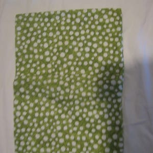 May include: A green fabric with a white polka dot pattern. The fabric is folded in half and has a smooth texture.