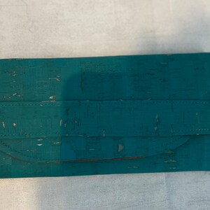 May include: A teal blue cork wallet with a stitched seam and a curved flap.