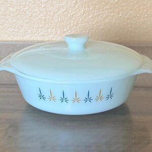 May include: A light blue glass casserole dish with a matching lid and two side handles. The exterior features a repeating horizontal pattern of small, star-like bursts in alternating dark blue and gold colors around the center of the bowl.