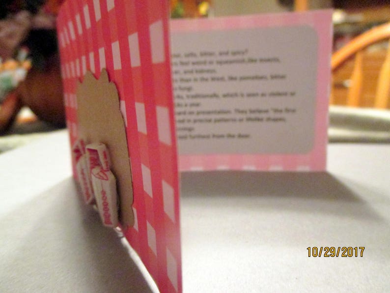 May include: A pink and white checkered card with a brown cutout and attached candy. The card is open, revealing text on a pink background. The date "10/29/2017" is visible.