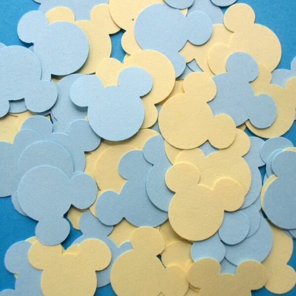 May include: A collection of light blue and pale yellow Mickey Mouse-shaped confetti scattered on a bright blue surface. The confetti is made of paper and is ideal for party decorations or craft projects.