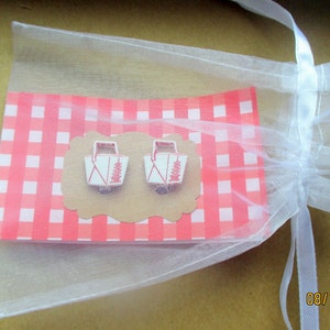 May include: A pair of white and red picnic basket earrings on a pink and white checkered background, presented in a sheer white gift bag. The earrings are on a brown, scalloped-edge card. The bag is tied with a white ribbon.