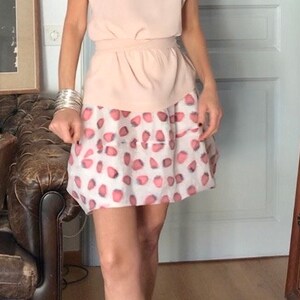 Può includere: Una donna indossa una blusa rosa e una gonna bianca con pois rosa e grigi.