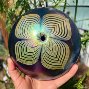 May include: A round, iridescent glass paperweight with a swirling, multi-colored pattern. The paperweight has a small hole in the center.