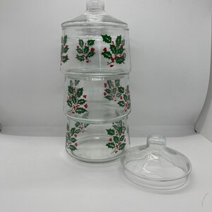 May include: A three-tiered glass candy jar with a holly and berry design. The jar has a clear glass lid.