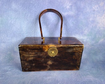 May include: A vintage-style rectangular handbag with a tortoiseshell effect. It has a curved handle and a decorative gold-coloured clasp. The bag's colour palette includes shades of brown and amber, creating a classic, retro appearance.