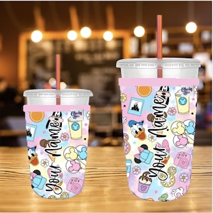 May include: Two clear plastic cold drink cups with pink and pastel-colored sleeves. The sleeves feature Disney character graphics, the text "Your Name", and other icons. Each cup has a pink straw.