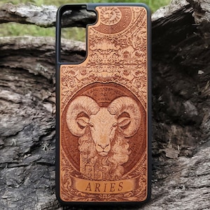 May include: A wooden phone case with a black border and a detailed design featuring the zodiac sign Aries. The design includes a ram's head with intricate details and the word "Aries" in a banner.
