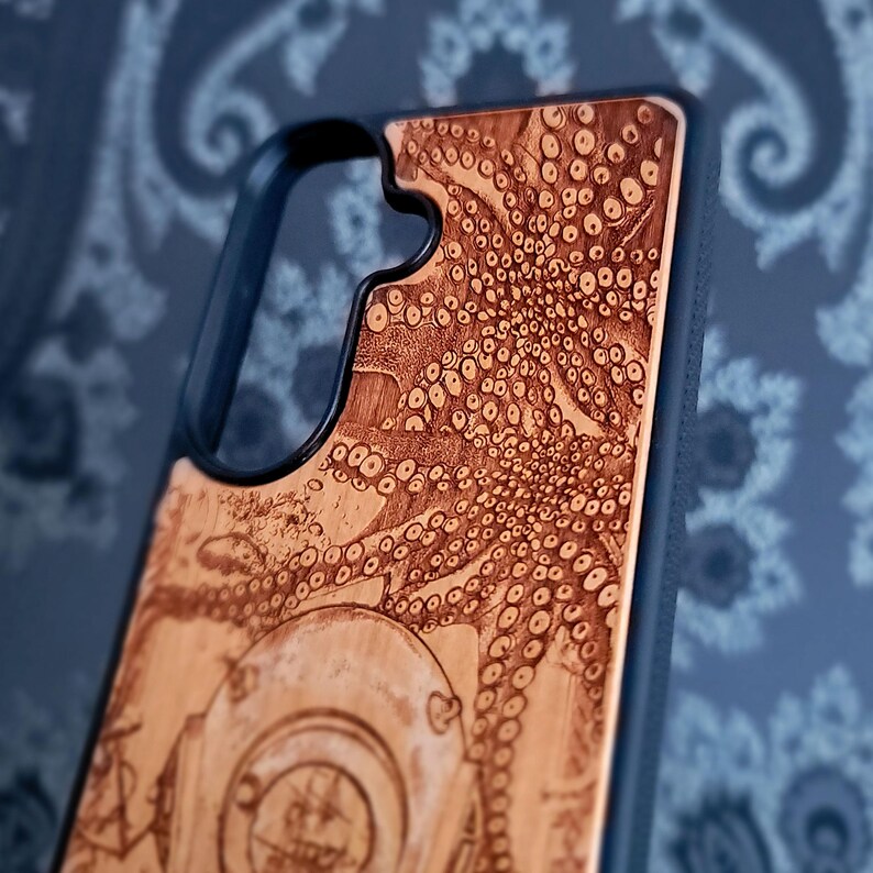 May include: A black smartphone case featuring a light brown wood inlay on the back. The wood surface is laser-engraved with a detailed illustration of an octopus with visible suction cups and a portion of a vintage diving helmet at the bottom.