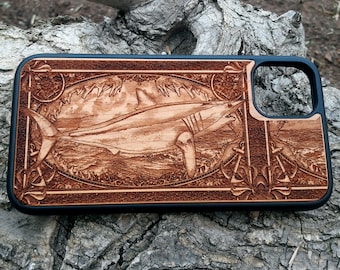 May include: A wooden phone case with a detailed carving of a shark. The case is black and has a cutout for the camera lens.