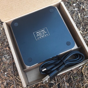 May include: A black wireless charger with a USB cable. The charger has a label that reads "WIRELESS CHARGER Input 5V/2A 9V/2A Output 5V/1A 9V/1.67A Made in China CE FC RoHS"