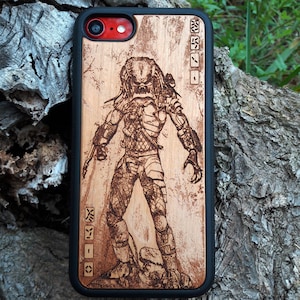 Peut inclure: Une coque de téléphone en bois avec une bordure noire et une image gravée au laser d'un personnage de Predator. La coque a un motif de grain de bois et le personnage de Predator est en position debout.