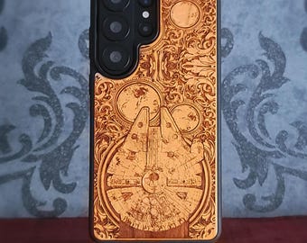 Puede incluir: Una funda de smartphone negra con un panel trasero de madera de color marrón claro que presenta un diseño grabado con láser de una nave espacial circular rodeada de intrincados patrones florales y dos pequeñas formas planetarias circulares.