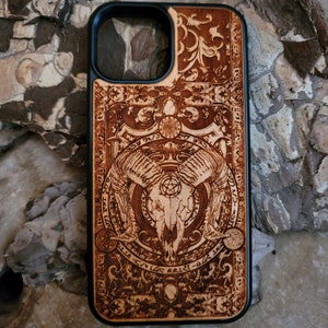 May include: A wooden phone case with a black border. The case features a detailed design of a skull with horns and a pentagram, surrounded by intricate patterns and symbols.