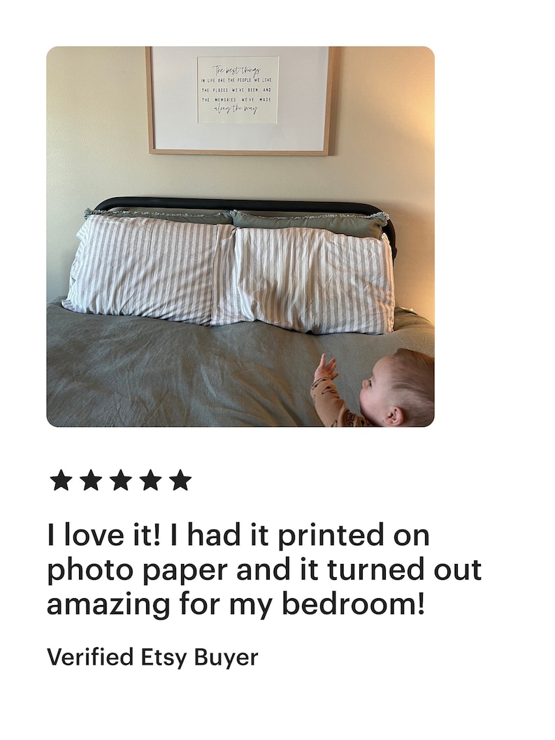 May include: A framed print with the text "The best things in life are the people we love, the places we've been, and the memories we've made along the way." The print is hanging on a wall above a bed with two pillows and a baby lying on the bed.