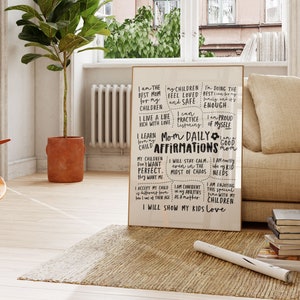 May include: A framed print with the text "Mom Daily Affirmations" in black script. The affirmations are in a handwritten style, with phrases like "I am the best mom" and "I will show my kids love." The print is displayed in a living room setting.