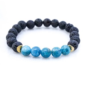 Può includere: Un braccialetto in pietra lavica nera e pietre blu con accenti dorati. Il braccialetto è fatto di perline rotonde ed è lungo circa 18 cm.