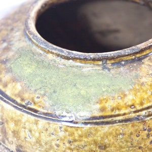 May include: A brown ceramic pot with a wide opening and a textured surface. The pot has a green glaze and a dark brown rim.