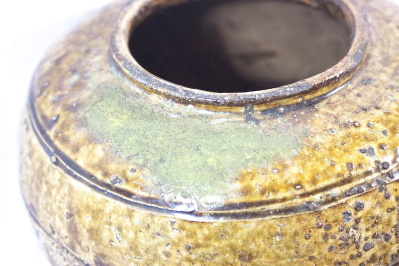 May include: A brown ceramic pot with a wide opening and a textured surface. The pot has a green glaze and a dark brown rim.