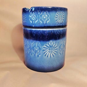 May include: A blue ceramic ashtray with a white and blue floral pattern. The ashtray has a lid.