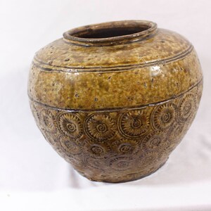 May include: A large, brown ceramic jar with a textured surface and a pattern of raised circles. The jar has a wide mouth and a rounded body.