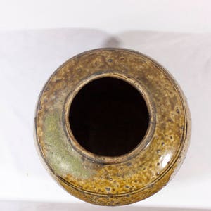 May include: A brown ceramic pot with a wide opening and a textured surface. The pot has a dark brown glaze with a speckled pattern.