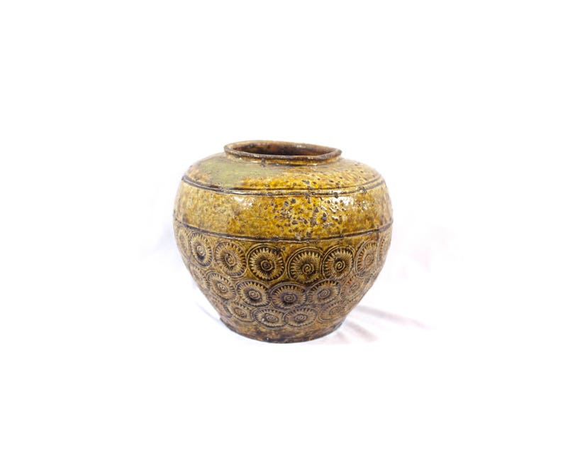 May include: A brown and yellow ceramic jar with a circular pattern. The jar has a wide mouth and a rounded body.