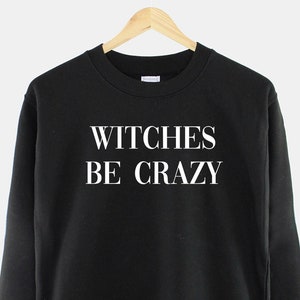Op de afbeelding: Zwart sweatshirt met witte tekst die "WITCHES BE CRAZY" zegt.