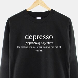 May include: Black sweatshirt with white text that reads "depresso [depresǝ] adjective the feeling you get when you've run out of coffee."