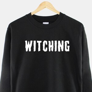 May include: Black sweatshirt with the word "Witching" printed in white on the front.