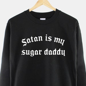 May include: Black sweatshirt with the text "Satan is my sugar daddy" in white gothic font.