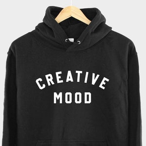May include: Black hooded sweatshirt with the text "CREATIVE MOOD" in white lettering.