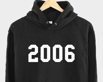 Pode incluir: Camisola de capuz preta com uma impressão branca do ano 2006.