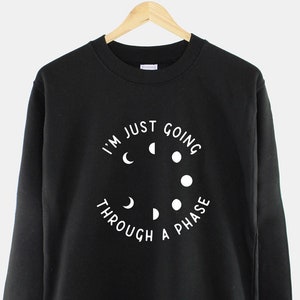May include: Black sweatshirt with a white graphic that says "I'm just going through a phase" with a circle of moon phases around the text.