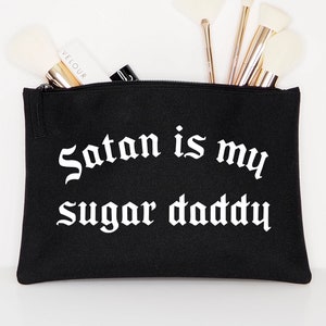 Op de afbeelding: Zwarte toilettas met rits met de tekst "Satan is my Sugar Daddy" in witte gotische letters.