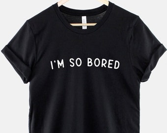 May include: Black t-shirt with white text that reads "I'M SO BORED" hanging on a wooden hanger.
