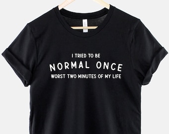 Op de afbeelding: Zwart T-shirt met witte tekst die luidt: "Ik heb geprobeerd om een ​​keer normaal te zijn. De slechtste twee minuten van mijn leven."